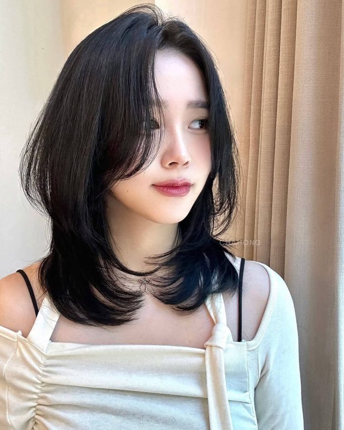 Asian model with layered black hair wearing white ruched top against beige curtain