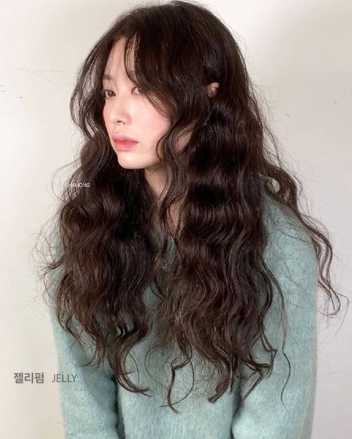 Asian model with long wavy black hair wearing mint green sweater against white background