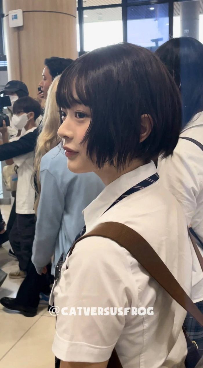 Asian model with short black bob wearing white uniform and brown bag in public space