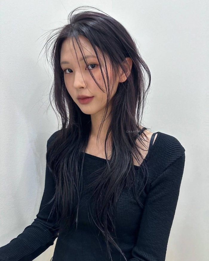 Asian model with tousled long black hair and wispy bangs wearing black ribbed sweater against white background