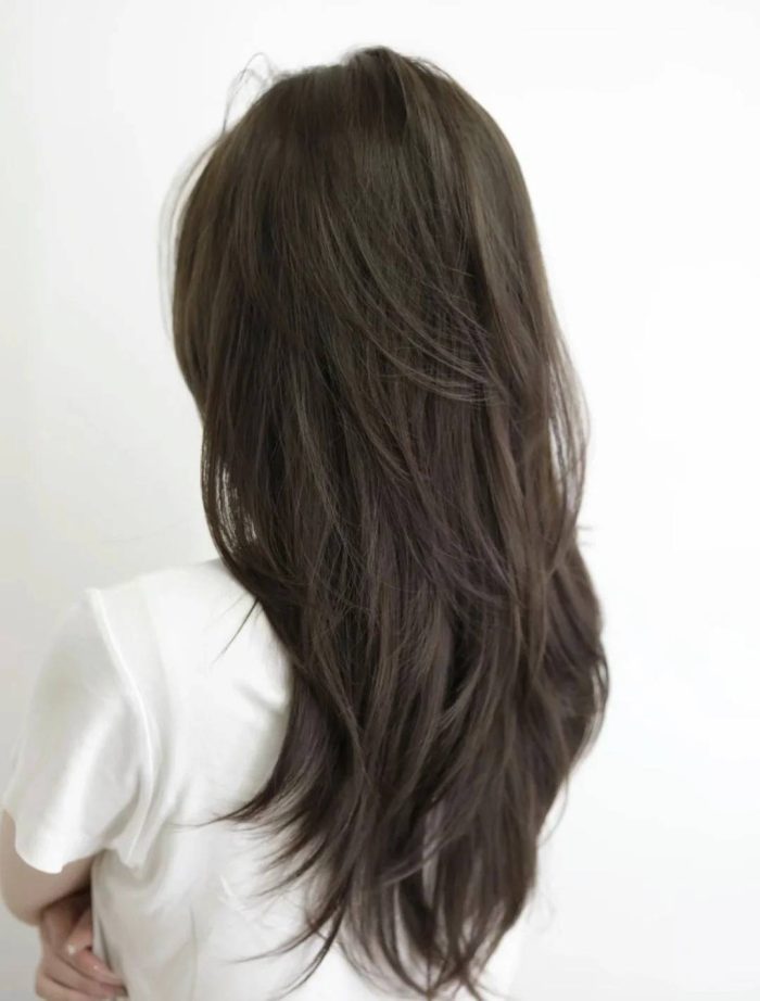 Back view of long layered dark hair wearing white top against white wall