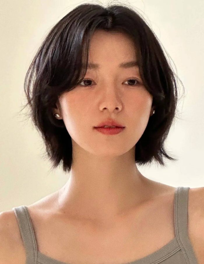 Short black layered bob hairstyle with curtain bangs and natural makeup look