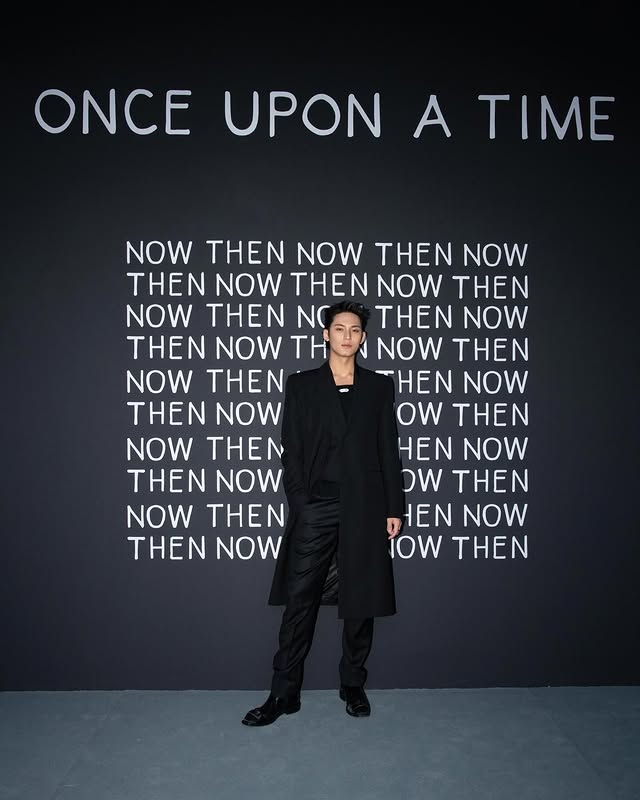 Asian male model in all-black outfit against dark backdrop with 'ONCE UPON A TIME' and 'NOW THEN' text wall