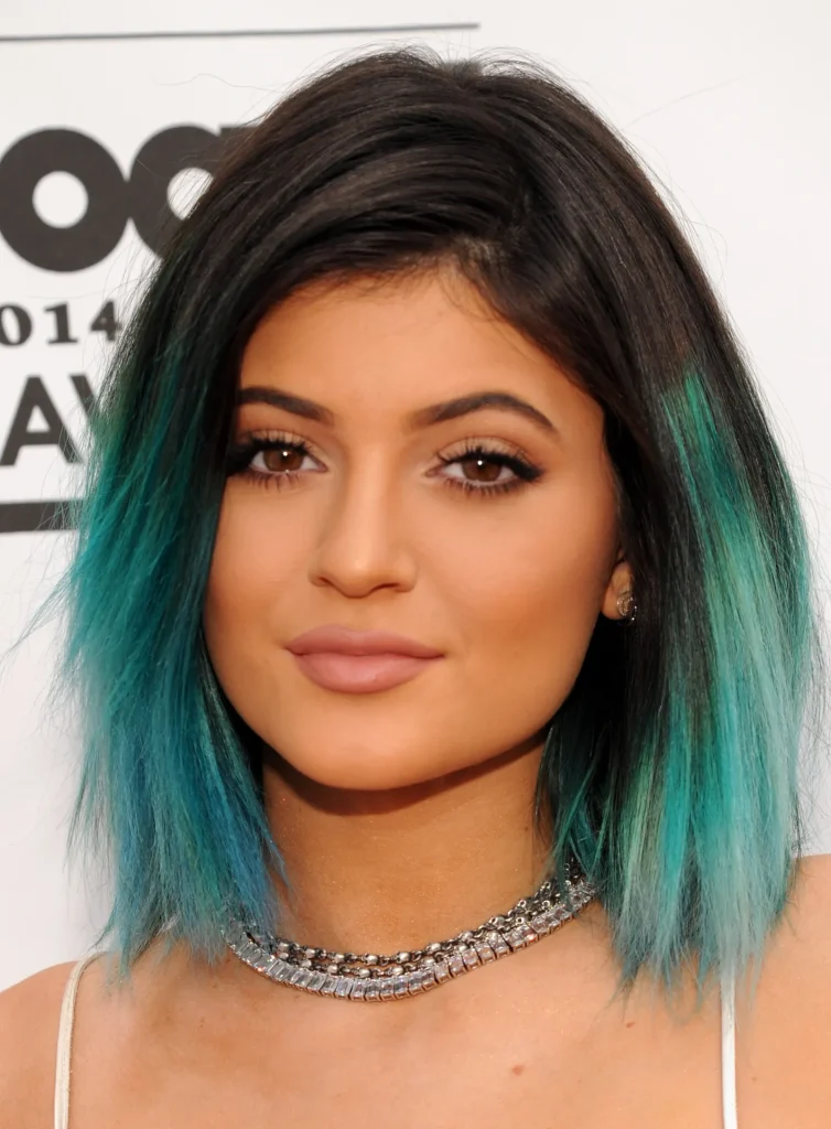 Celebrity with black to teal ombre hair wearing crystal necklace at awards event