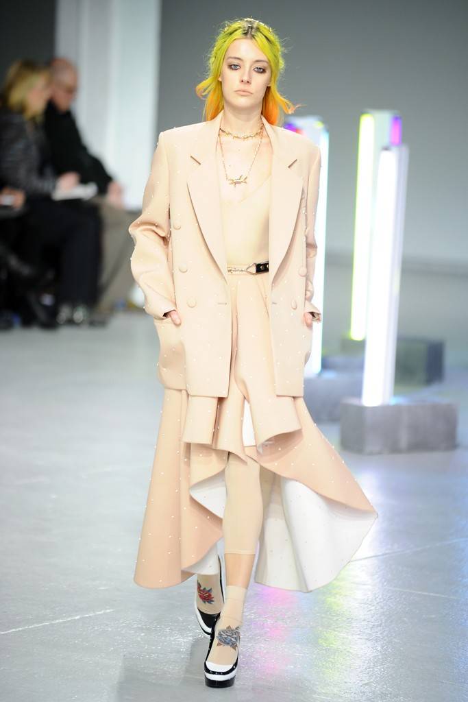 Model with neon yellow hair wearing cream oversized blazer and asymmetrical skirt ensemble on modern runway