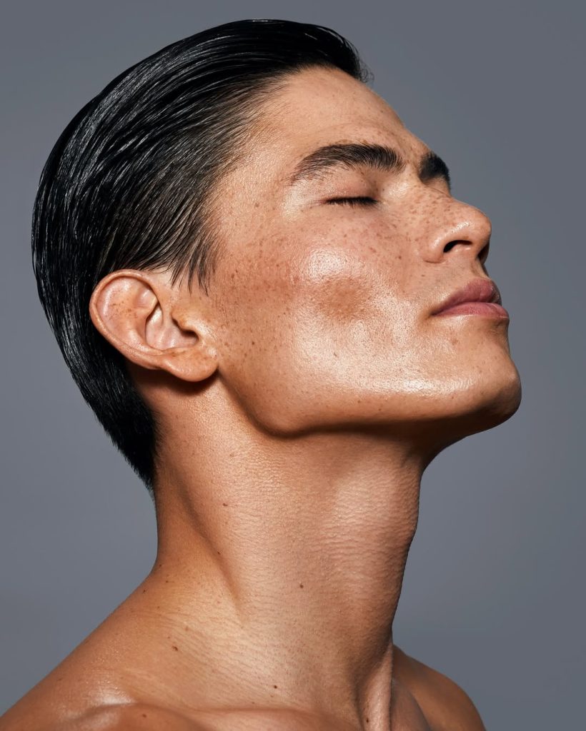 Close-up profile of Asian male model with slicked back hair and dewy skin against gray backdrop