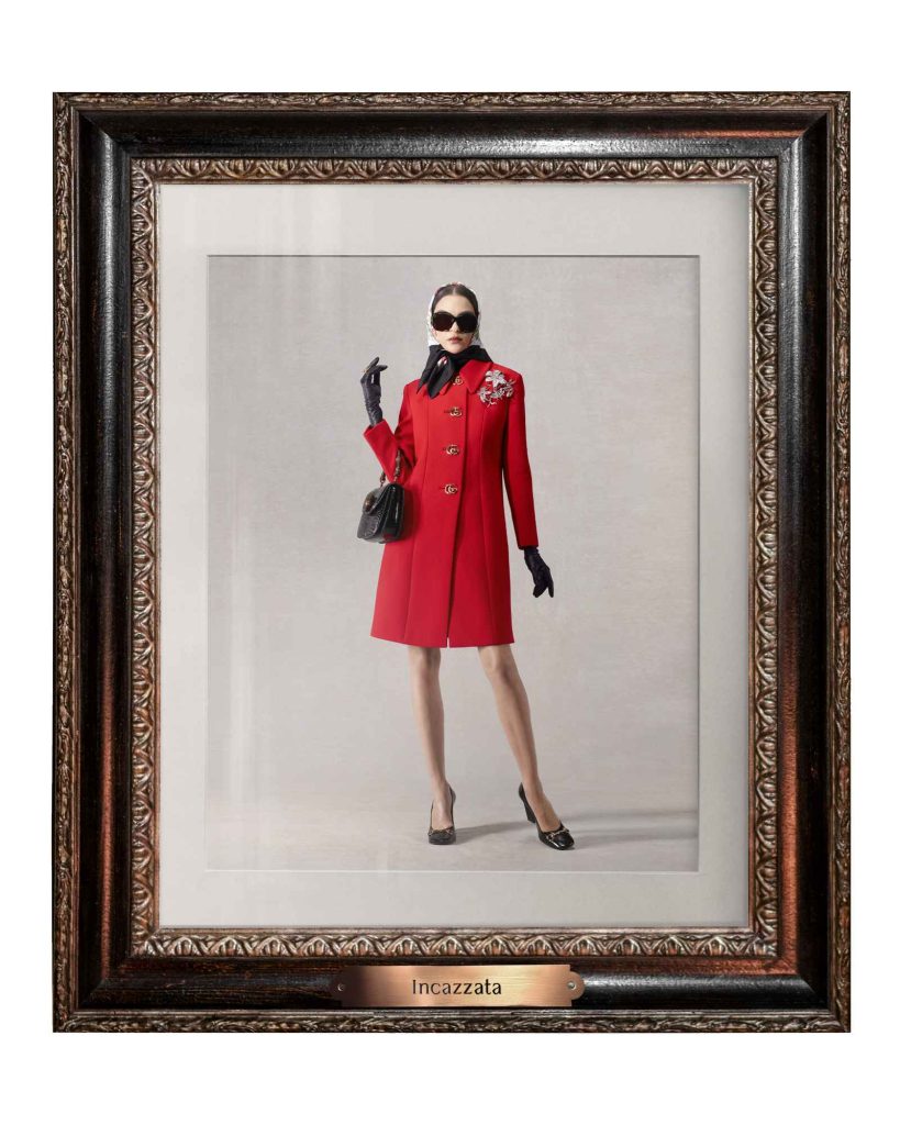 Model in classic red coat dress with black accessories including gloves, sunglasses, and handbag, posed elegantly in ornate vintage frame labeled Incazzata